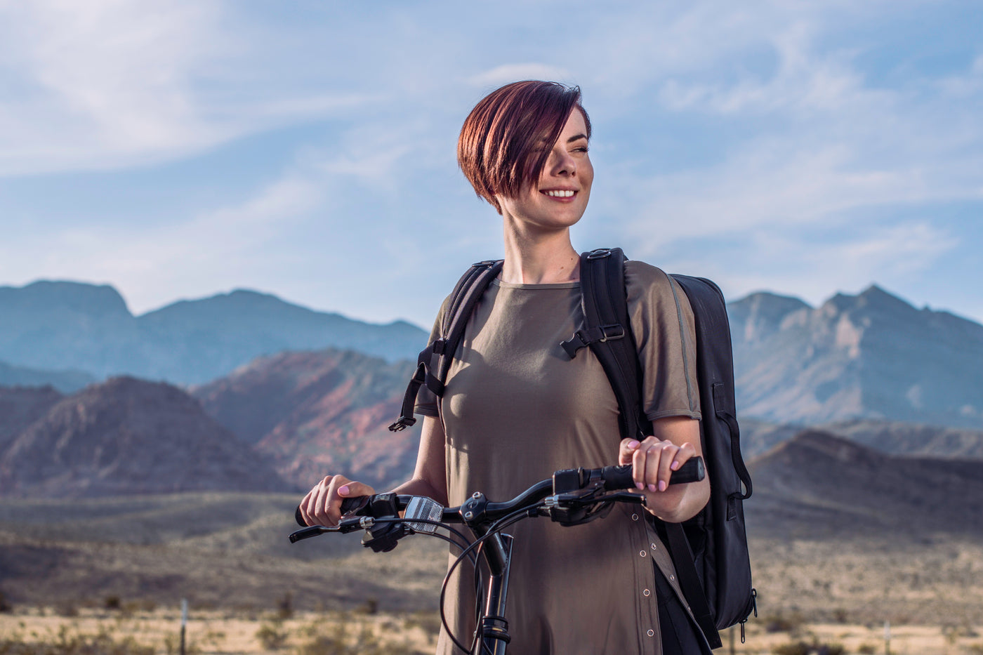 Woman on bike wearing a backpack and Splice Clothing reversible travel clothing while smiling in front of Red Rock Canyon, Las Vegas, Nevada