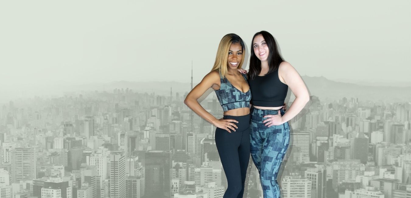 Two women posing together wearing Splice Reversible Travel Clothing opposite matching outfits including Empire Reversible Leggings and Empire Reversible Bra Top in front of New York cityscape background